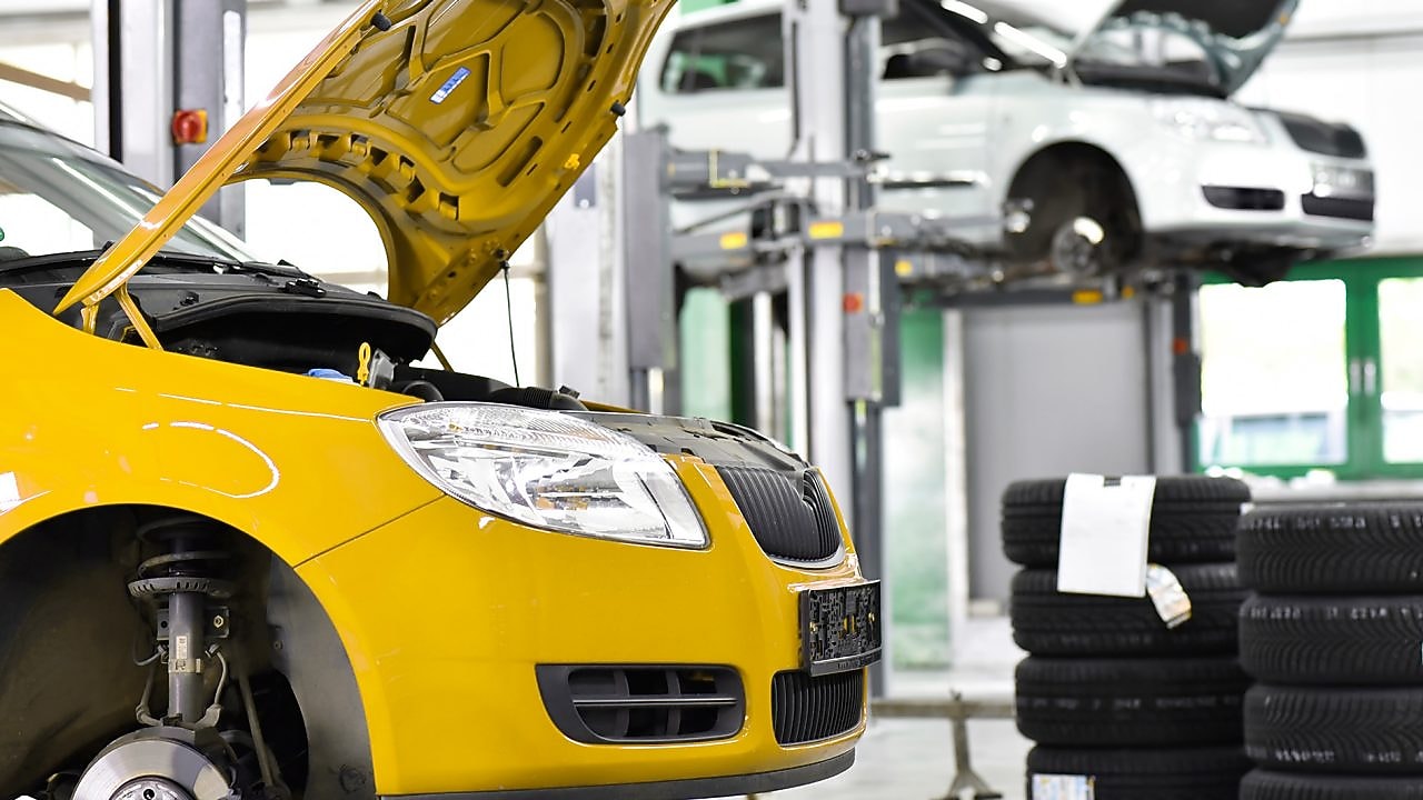 two cars in a garage, one yellow and one white, with their bonnets open, and some car tyres in the background