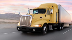 A yellow truck driving down a road at dusk