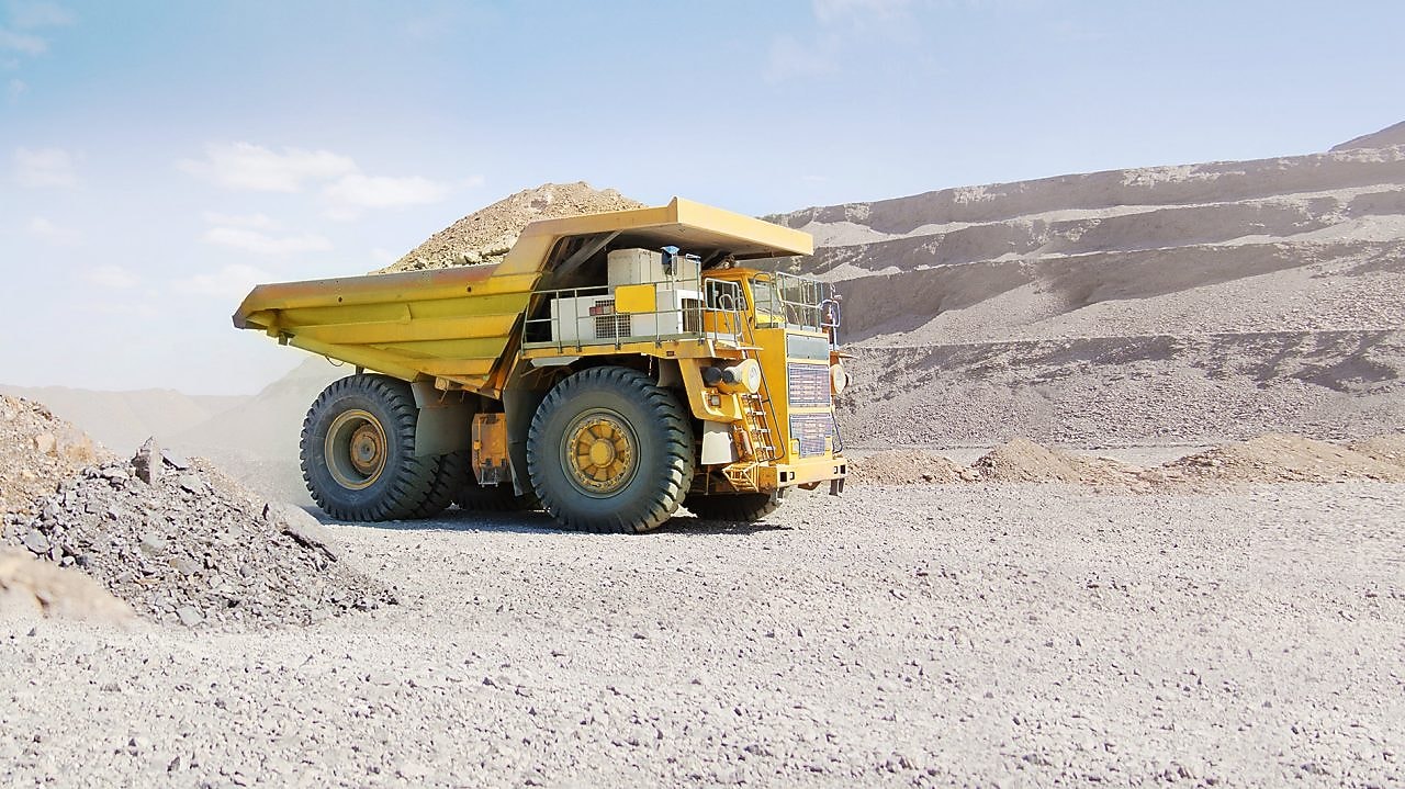 yellow dumper truck driving through gravel