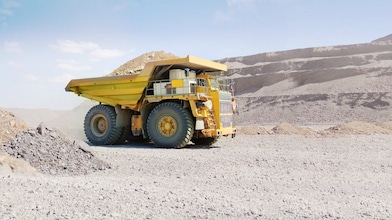 yellow dumper truck driving through gravel