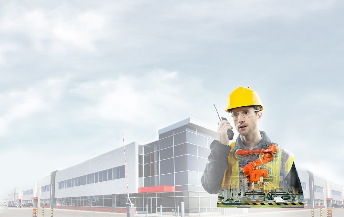 A man with yellow hard hat speaking into a radio transposed on a background showing a large building