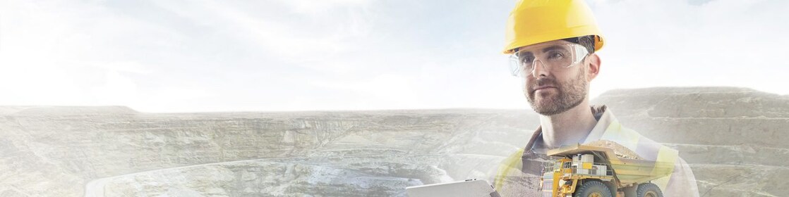 worker in yellow hard hat transposed onto a background of cliffs and a large yellow truck